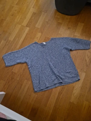 Blåmelerad stickad tröja - En blåmelerad stickad tröja med  avslappnad passform och trekvartsärmar. Tröjan har rund halsringning och är tillverkad i ett mjukt, grovt stickat material. Perfekt för en chill och stilren look.