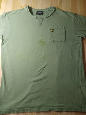Grön t-shirt från Lyle & Scott - Snygg grön t-shirt från Lyle & Scott Junior med rund halsringning och bröstficka med den klassiska gula loggan. T-shirten har korta ärmar och är tillverkad i mjuk bomull, perfekt för en avslappnad stil. Med en smutsig fläck