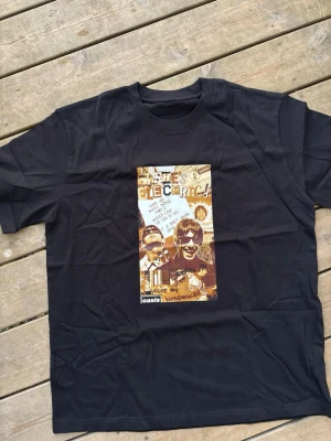 Svart Oasis t-shirt med tryck - Cool svart t-shirt med stort grafiskt tryck på framsidan inspirerat av Oasis och låten Wonderwall. Trycket har collage-stil med text och bilder i bruna och beige toner. Klassisk rund hals och korta ärmar. Perfekt för dig som gillar bandtröjor och musikstil. 