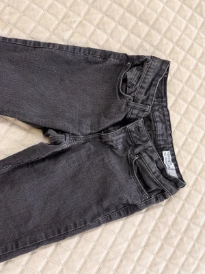 Svart/gråa lågmidjade utsvängda jeans från vero Moda - Ett par svart/gråa jeans med lågmidja och utsvängda ben. Klassisk femficksmodell med bälteshällor och knappgylf. Jeansen är i ett mjukt denimtyg som ger en avslappnad och trendig look.