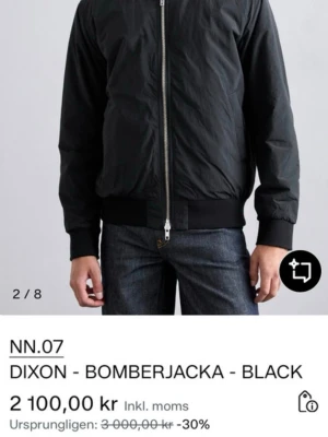 Svart bomberjacka från NN.07 - Stilren svart bomberjacka från NN.07 med klassisk rak passform, ribbade muddar vid ärmslut och midja samt dragkedja framtill. Jackan har en minimalistisk look och är tillverkad i ett lätt, slätt material som ger en modern vibe.