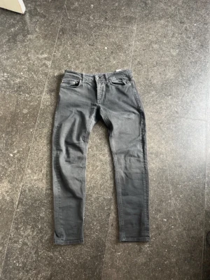 Svarta Dondup jeans - Säljer ett par gråa/svarta jeans från Dondup med snygga detaljer som metallknappar och logotyp på bakfickan. Jeansen har slim passform och är tillverkade i ett mjukt denimtyg som sitter skönt.