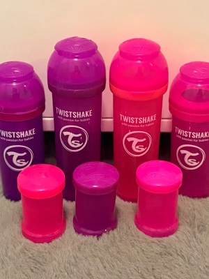 Twistshake nappflaskor och dinappar plus rabattkuponger  - Säljer ett set med fyra Twistshake nappflaskor i lila och rosa plast samt tillhörande förvaringsbehållare. Medföljer även fyra förpackningar med Twistshake anti-kolik dinappar i storlek S och M. Perfekt för dig som vill ha extra flaskor och nappar till bebis. Skickar även med Rabattkuponger som jag inte kommer att använda. Flaskorna är använda och har inga Dinappar med än dom nya i förpackningen 