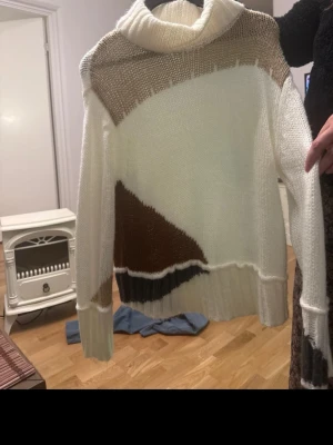 Stickad polotröja i beige och brunt - Säljer en oversized stickad polotröja med bred krage. Tröjan har ett coolt blockmönster i vitt, beige, brunt och svart. Långa ärmar och ribbade muddar. Perfekt för dig som gillar en avslappnad och trendig stil.