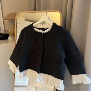 Mörkgrå kofta med utstickande skjorta - Snygg mörkgrå kofta med rund hals och utstickande vit skjorta i ärmarna och nertill. Delarna sitter ihop. Passar större och mindre. Supersnygg och minimalistisk. 