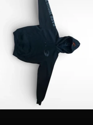 Svart hoodie från Gaso Industries - Svart hoodie från Gaso Industries med tryck på ena ärmen och en logga på bröstet. Klassisk känguruficka framtill och justerbar huva med snören. Perfekt för en avslappnad streetwear-look. Materialet ser ut att vara mjuk bomullsblandning.