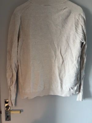 Beige ziptröja från Kappahl - Ljusbeige ziptröja från Kappahl med ribbade muddar och krage. Tröjan har dragkedja framtill och är tillverkad i ett mjukt, stickat material. Perfekt för lager på lager och enkel att matcha med olika outfits.