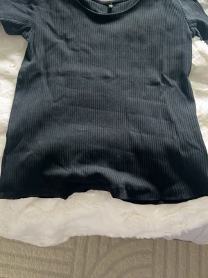 Svart ribbad topp med kort ärm - En enkel och stilren svart ribbad topp med korta ärmar och rund hals. Perfekt att matcha med jeans eller kjol för en clean look. Mjuk och stretchig känsla som sitter snyggt på kroppen.