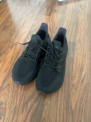 Svarta Adidas Ultraboost sneakers - Säljer ett par helsvarta Adidas Ultraboost sneakers med stickad ovandel och klassiska tre ränder på sidan. Perfekta för dig som gillar stilrena och bekväma sneakers i sportig design.Nypris är 2000 kr
