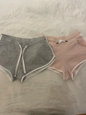 Två par mjukisshorts med snörning - Dom rosa shortsen är ifrån h&m i storlek 140, dom gråa är ifrån newyorker i storlek xs. Säljer båda shortsen för 25kr tillsammans. Säljer 2 par mjukisshorts i färgerna grå och rosa med vita kanter och snörning i midjan. Perfekta för sommaren och riktigt sköna att chilla i. Klassisk sportig look och tillverkade i mjukt bomullsmaterial. 