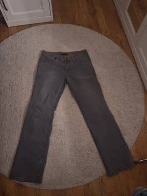 Gråa raka jeans - Säljer ett par gråa jeans med rak passform och klassiska fem fickor. Jeansen har diskreta slitningar och kontrastsömmar. Tillverkade i ett robust denimtyg som passar perfekt till en avslappnad stil.