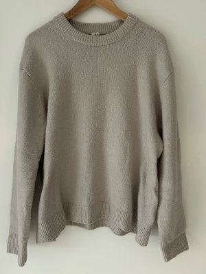 Beige stickad tröja från Arket  - En enkel och stilren beige stickad tröja med rund halsringning och ribbade muddar vid ärmslut och nederkant. Tröjan har en avslappnad passform och är perfekt för lager på lager. Materialet känns mjukt och bekvämt mot huden. Tröjan är köpt från Arket för 790kr men säljer den för 450kr då den är helt oanvänd. 