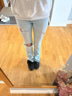 Ljusblå slitna jeans med hål - Säljer ett par ljusblå jeans med slitningar och stora hål vid knäna. Jeansen är bootcut och har klassiska bakfickor med lock och knapp. Perfekta för en avslappnad och trendig look. Storleken är 170 men passar mig som brukar ha xs-s 💕