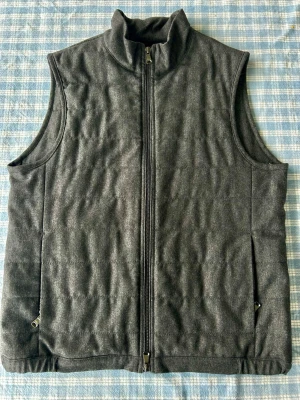 Mörkgrå quiltad Ullväst - Stilren mörkgrå ullväst med quiltad design och hög krage. Västen har hel dragkedja framtill och två sidofickor med dragkedja. Perfekt för lager-på-lager och enkel att matcha till olika outfits.