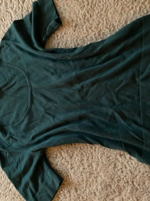 Mörkgrön stickad t-shirt från Peter Hahn - En enkel och stilren mörkgrön stickad t-shirt från Peter Hahn. T-shirten har rund halsringning och korta ärmar. Tillverkad i mjukt bomullsmaterial som känns skönt mot huden. Perfekt basplagg att matcha med olika stilar.