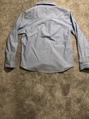 Ljusblå klassisk skjorta - En ljusblå skjorta med klassisk krage och vita knappar framtill. Skjortan har en bröstficka och långa ärmar med knapp vid manschetten. Perfekt till jeans eller chinos för en clean look.