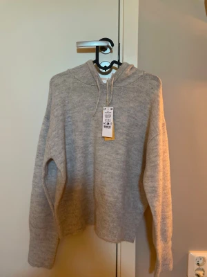 Ljusgrå stickad hoodie med huva - Mysig ljusgrå stickad hoodie från Gina tricot med huva. Tröjan har avslappnad passform, ribbade muddar och är tillverkad i mjukt material som passar perfekt för chill dagar. Enkel och stilren design som funkar till det mesta.