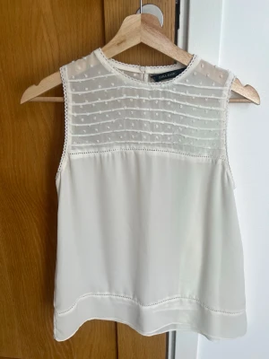 Söt vit ärmlös blus från Zara Basic - Söt vit blus från Zara Basic med transparent mesh upptill och små prickdetaljer. Ärmlös modell med rund halsringning och dekorativa spetskanter. Perfekt att styla med jeans eller kjol för en fräsch look.