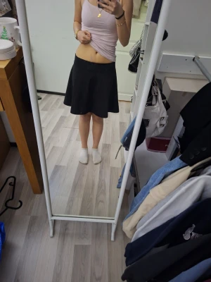 Svart kortkjol  - Säljer en enkel och stilren svart kortkjol. Kjolen har en mjuk och lätt utsvängd passform som ger en snygg siluett. Perfekt att matcha med olika toppar för en trendig look. Använd ändast nån gång.