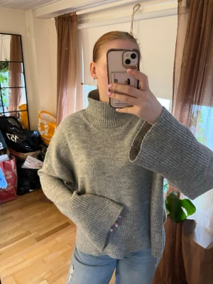 Grå oversized polotröja - Mysig grå stickad polotröja med oversized passform och vida ärmar. Tröjan har ribbstickade detaljer vid ärmslut, nederkant och krage. Perfekt för lager-på-lager och chill dagar.