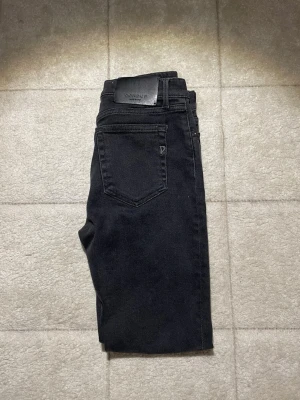 Svarta jeans från Dondup - Säljer ett par svarta jeans från Dondup med klassisk femficksdesign och snyggt läderpatch bak. Jeansen har raka ben och är tillverkade i ett mjukt denim-material som känns bekvämt. Perfekt för dig som gillar stilrena och tidlösa jeans.