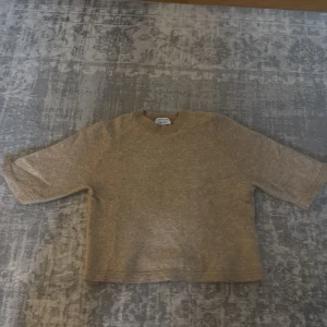 Beige stickad t shirt från & Other Stories - Mysig beige stickad T-shirt från & Other Stories Stockholm Atelier. Tröjan har rund halsringning, ribbade muddar och en avslappnad passform. Perfekt för lager på lager och enkel att matcha med olika stilar.