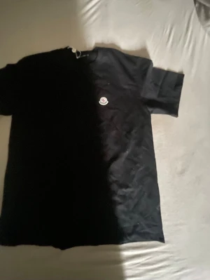 Svart Moncler t-shirt i bomull - Snygg svart t-shirt från Moncler med klassisk passform och rund hals. T-shirten har Monclers ikoniska logga broderad på bröstet och är tillverkad i mjuk bomull. Perfekt för dig som gillar stilrena och exklusiva plagg.