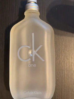 CK One parfym från Calvin Klein - Minimalistisk och stilren parfymflaska från Calvin Klein, CK One. Flaskan är frostad och genomskinlig med silverfärgad skruvkork och tydlig logga på framsidan. Passar dig som gillar klassisk och fräsch doft i en ikonisk design. 100ml flaska med cirka 80-85ml kvar