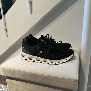 Svarta On Running sneakers - Snygga svarta sneakers från On Running med vit och svart sula. Skorna har en sportig design med meshmaterial för bra ventilation och klassiska snörningar. Märkets logga syns på sidan och hälen. Perfekta för dig som gillar stilrena och bekväma sneakers. Org pris 1799kr