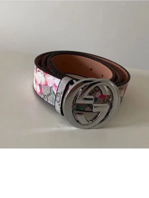 GG blommigt bälte med silverdetaljer - Snyggt bälte från  med blommigt mönster i rosa, grönt och vitt. Bältet har en stor, rund spänne i silver med GG-logga och är gjort i skinn. Perfekt accessoar för att lyfta din outfit.