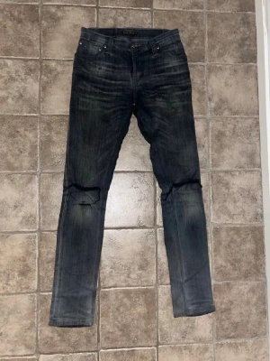 Nudie jeans - Nudie jeans i grå tvätt med snygga slitningar och hål vid knäna. Modellen är slim och har klassisk femficksdesign. Jeansen är i stretchigt denim och passar dig som gillar en smalare siluett med lite edge.Obs modellappen ej kvar. Midja 35cm, längd 103cm. JAG SKICKAR EJ FLER BILDER NÄR JAG BÄR JEANSEN! för storleksguide hänvisar jag till måtten och för bättre inblick i passformen rekommenderar jag att googla på modellnamnet. kolla måtten noggrant :) 45