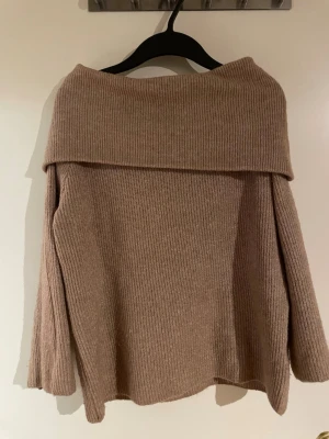 Beige off shoulder stickad tröja - Säljer en beige stickad tröja med bred off shoulder-krage och långa ärmar. Tröjan har en ribbad struktur och är i mjukt material, perfekt för en chill och trendig look. Passar till både jeans och kjol.