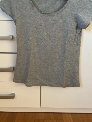 Grå basic t-shirt med rund hals - En enkel och stilren grå t-shirt med rund halsringning och korta ärmar. T-shirten har en normal passform och är tillverkad i mjuk bomull, perfekt för en clean och avslappnad look.