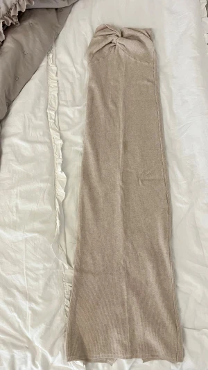 Beige ribbad långkjol med slits - Trendig beige långkjol i ribbat material med snygg knutdetalj i midjan och hög slits bak. Kjolen har en rak passform och är perfekt för dig som gillar en stilren och enkel look.