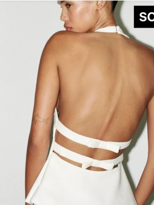 Backless top - Snygg vit halterneck topp med öppen rygg och breda band som knyts baktill. Toppen har en figurnära passform upptill och faller ut något nedtill. Perfekt för dig som vill sticka ut med en modern och trendig look.