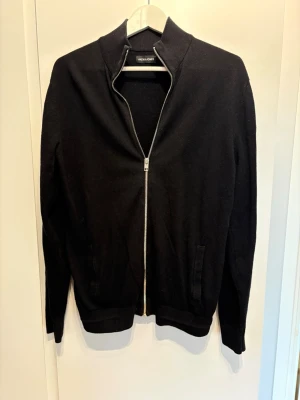 Svart ziptröja från Jack & Jones - Svart ziptröja från Jack & Jones med hög krage och hel dragkedja framtill. Storlek L men passar som M! Nytt skick.