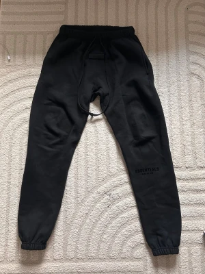 Svarta Essentials mjukisbyxor - Storlek:S Obs!! är oversized så kan passa M också.🔥                                                           Skick:Helt ny(påse tillkommer)💙.          Beskrivning:Säljer ett par svarta mjukisbyxor från Essentials.( Fear of god kollektionen).Byxorna har dragsko i midjan, muddar vid bensluten och diskret logga på benet. Tillverkade i mjukt och bekvämt material, perfekta för chill dagar.🌳☀️🌧️