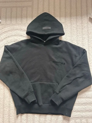 Svart Essentials Fear of God  - Storlek:storlek XXS men är oversized så rekommenderar att du bär S❄️.                 Skick:Extremt bra, bara använd ett par gånger.(påse tillkommer)💙                                                           Beskrivning:Svart hoodie från Essentials Fear of God med broderad logga på bröstet. Klassisk passform med huva och känguruficka framtill. Tjockt och mjukt material som känns lyxigt och street. Perfekt för dig som gillar stilrena och trendiga plagg.🔥