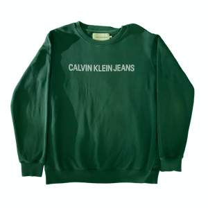 Snygg grön crewneck tröja från Calvin Klein Jeans i okej skick.  Har hittat en fläck (se bild tre) på framsidan vänster hörn nedtill. Men inte något vidare synligt slitage utöver det. Strlk XL.