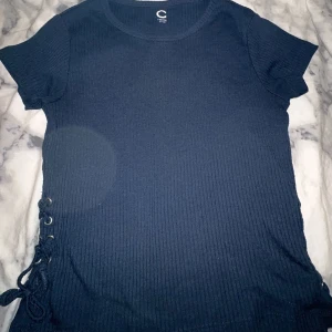 T-shirt  - Marinblå T-shirt med knytdetlajer på sidorna. Den är även ribbad och köpt från Cubus. Storlek 146-152 men funkar som Xs.