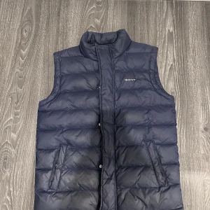 Gant väst  - Perfekt väst inför hösten köpt på gants butik i Gränby Uppsala! Den är i bra skick 8/10. Str 158/164cm, 13-14 år, perfekt i kallare väder då den är tjock och varm. Köparen står för frakten, tveka inte om du har någon fråga📦