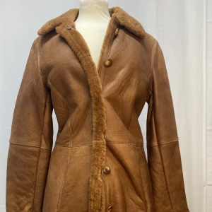 Skinnjacka - Äkta fårskinn, handgjord i Tyskland. Jackan har en vintage ”look” men är helt ny. Den är längre än på bilden, skulle säga att den går till knävecken. Väldigt varm med ull inuti. Den är storlek 42 men skulle säga att den passar mindre storlekar också.  