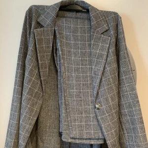 Matchande set (Blazer + kostymbyxor) - Helt nya. Aldrig använt. Snygg grå rutiga kostymbyxor och matchande blazer/kavaj. Båda plaggen är i storlek 38/M/UK10
