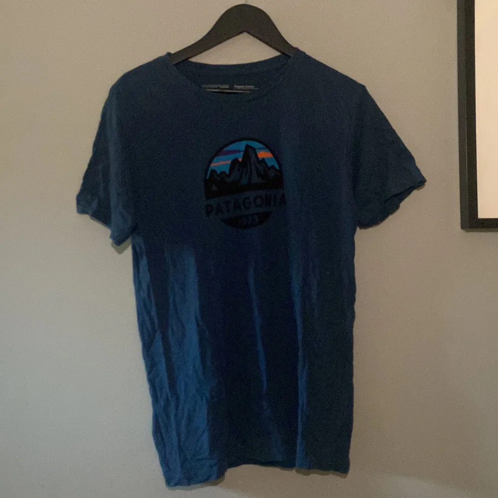 Marinblå Patagonia t-shirt med cirkulärt tryck på bröstet Modell: Slim fit  Nypris: 400kr. T-shirts.