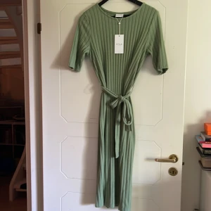 Grön ribbad klänning - Aldrig använd grön ribbad klänning från Vila. Knytband runt midjan