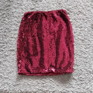 Kjol med paljetter - Kort vinröd kjol med paljetter. Kjolen är aldrig använd och i nyskick. Storleken är XS och den kommer från bubbleroom.  Betalning sker via swish och köparen står för frakten. 