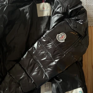 Svart dunjacka - Svart dunjacka. Köpte själv second hand så kan inte garantera att den är äkta. Använt skick. Storlek 1, skulle säga XS. Finns en luva till, men dragkedjan är sönder så kan behöva lagas om den ska fästas. Jättesnygg och varm!!! Många intresserade, buda!!!!