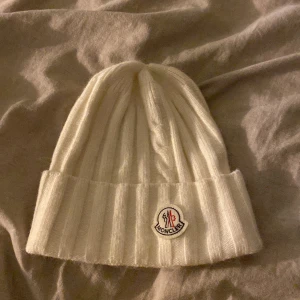 Moncler mössa vit - Vit moncler mössa säljer för jag använder ej längre!💗 och tröttnat på modellen😊 finns inga fläckar eller missfärgningar! Som oanvänd 