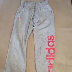 Gråa mjukisbyxor från adidas - Grå mjukisbyxor från Adidas med rosa logga på ena benet. Väl använda (se bild 3) men har fortfarande mycket att ge! 