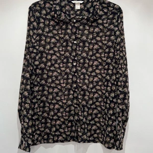 Blus  - Superfin blommig blus.  Blusen har rundad krage med volangkant. 